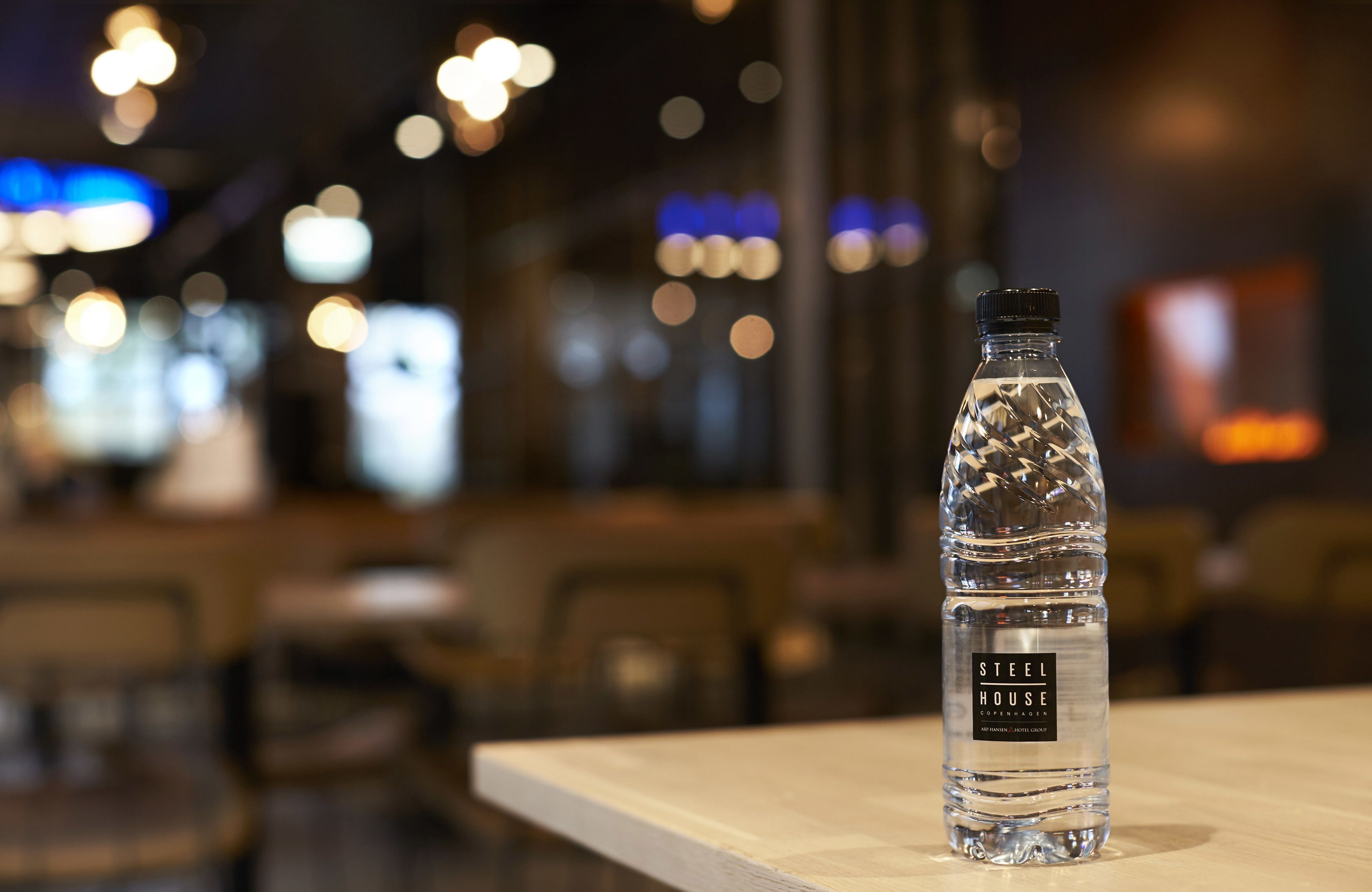 A clear water bottle labeled "Steel House" on a wooden table in a dimly lit indoor setting.