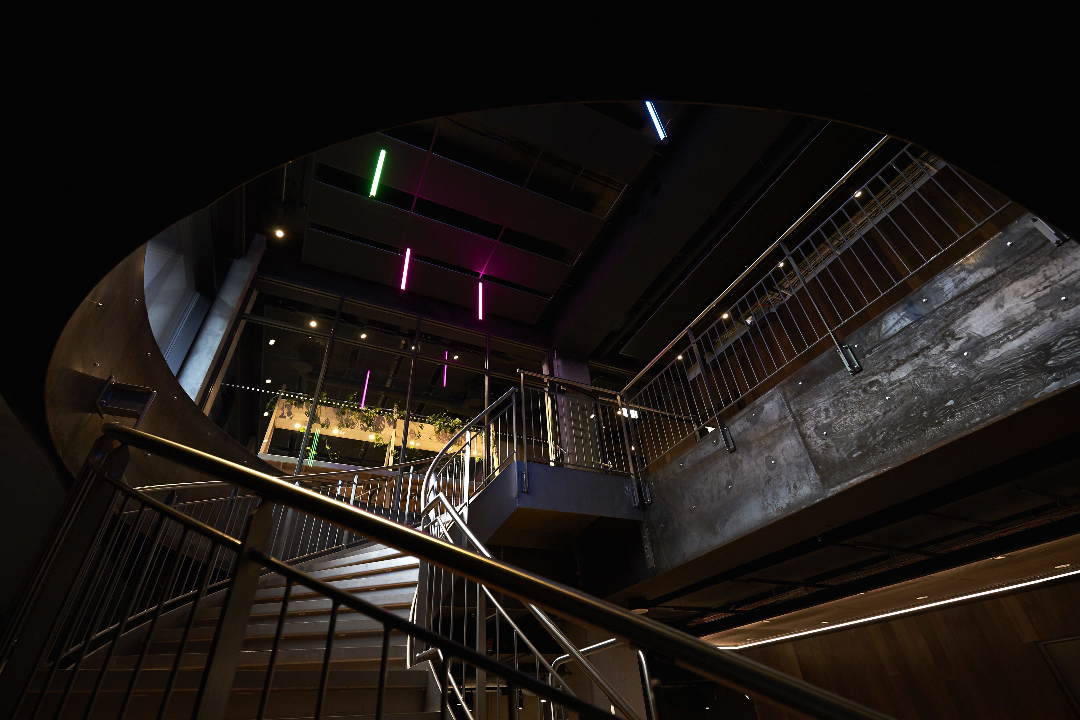 Un interno a più livelli con una scala a forma di ferro, ringhiere in metallo, un soffitto con travi a vista e corpi illuminanti.