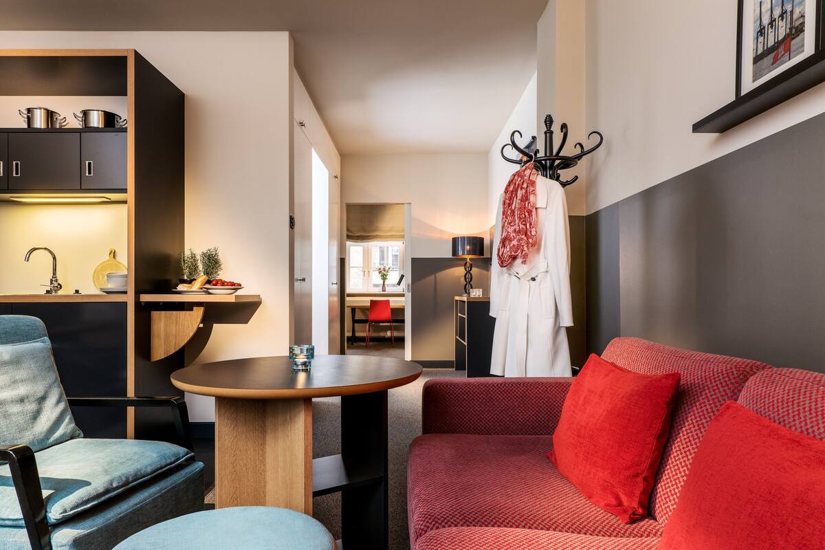 Un espacio habitable compacto con kitchenette, comedor y zona de estar con sofá y sillas.