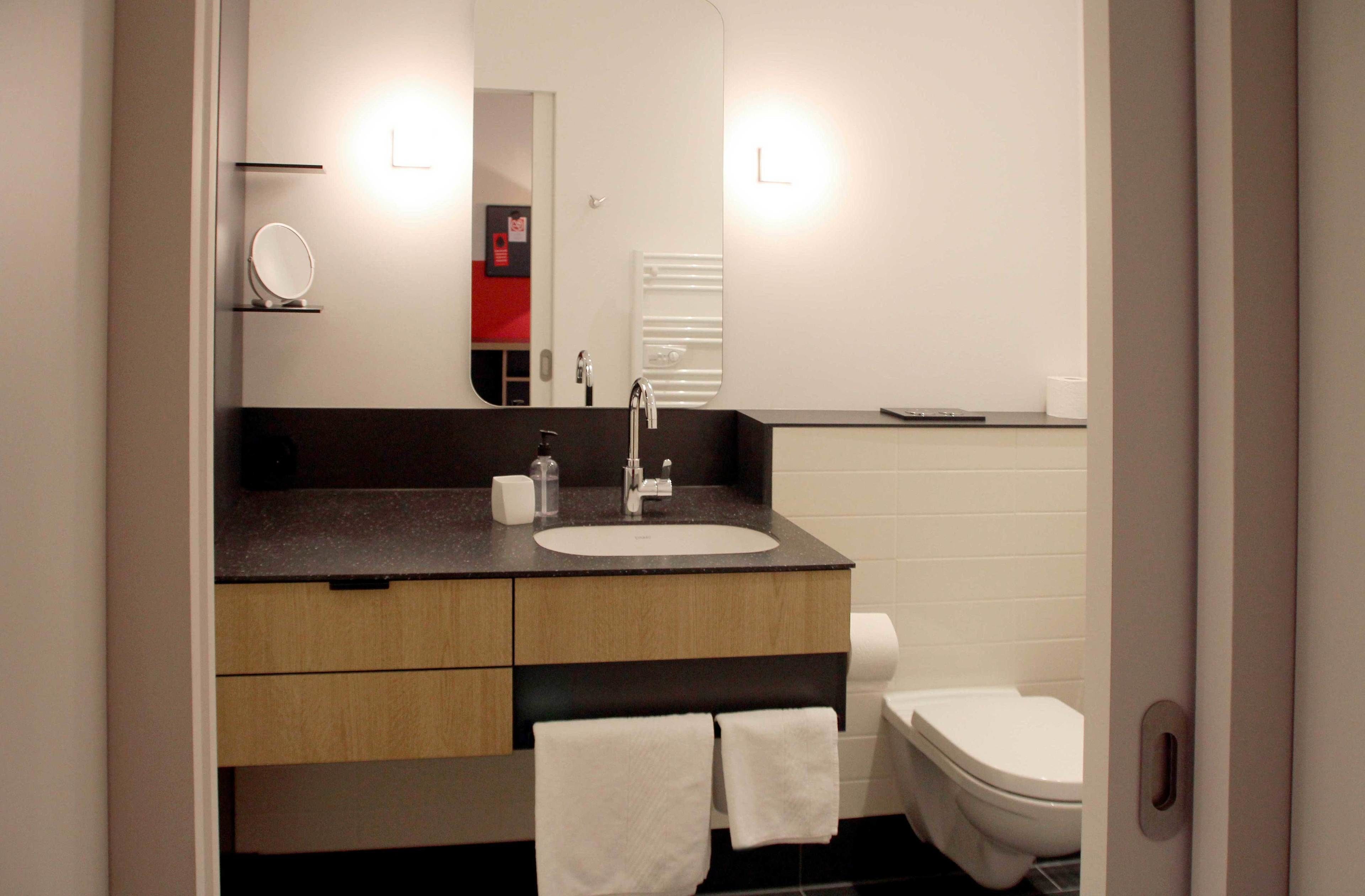 A modern bathroom with a dark countertop, a white sink, a mirror, a towel rack, and a toilet.