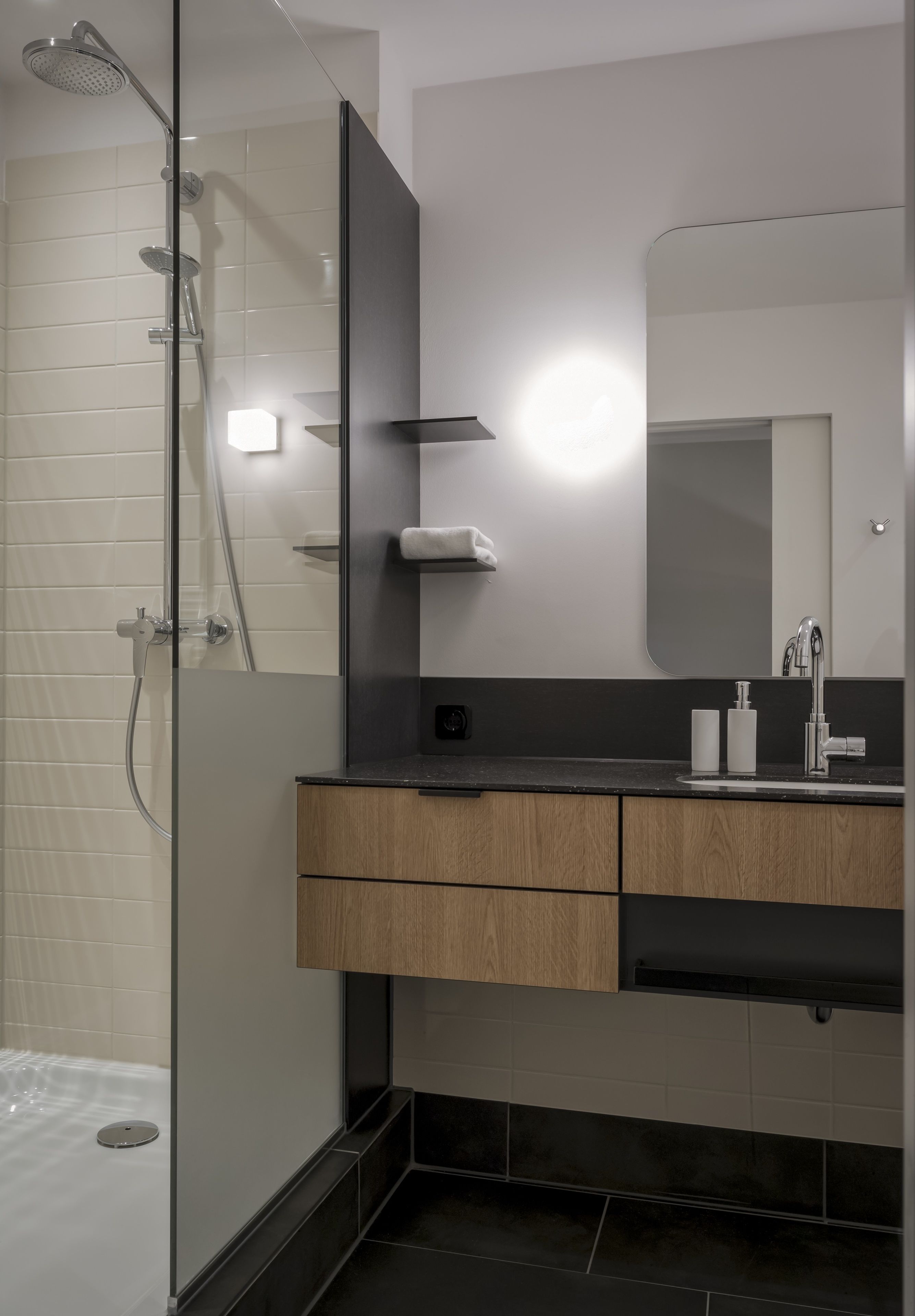 A modern bathroom with a glass-enclosed shower, a wooden vanity with a mirror, and a black countertop.