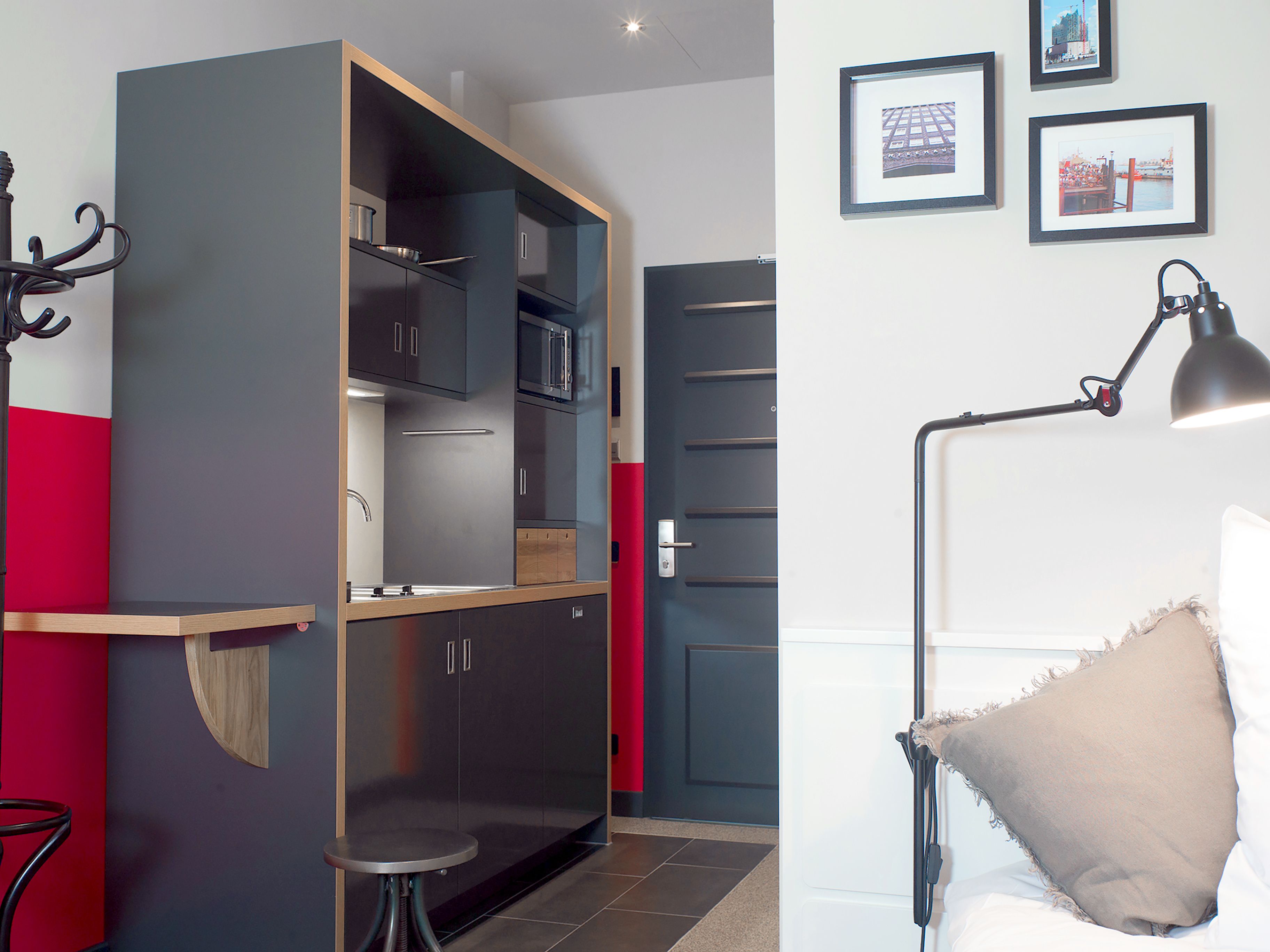 A compact kitchen with modern appliances, a dining area with a small table, and a bedroom with a bed and a nightstand.