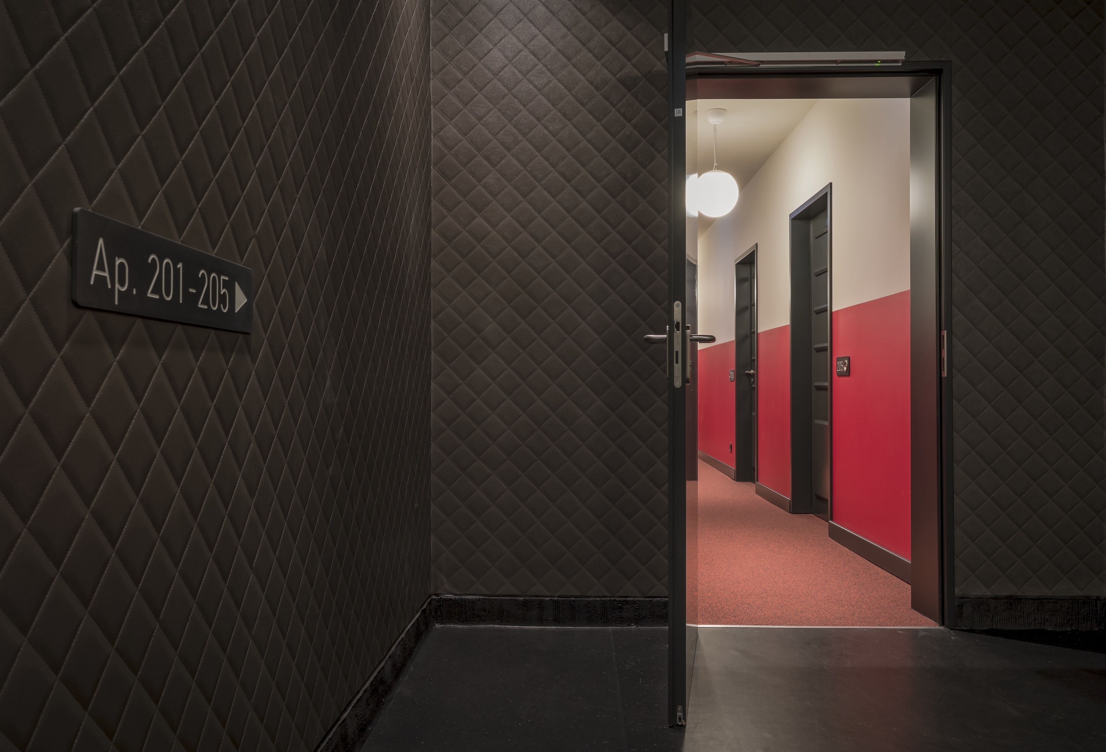 Pasillo con un cartel que indica los números de habitación 201 a 205, que conduce a un corredor rojo y blanco con puertas.