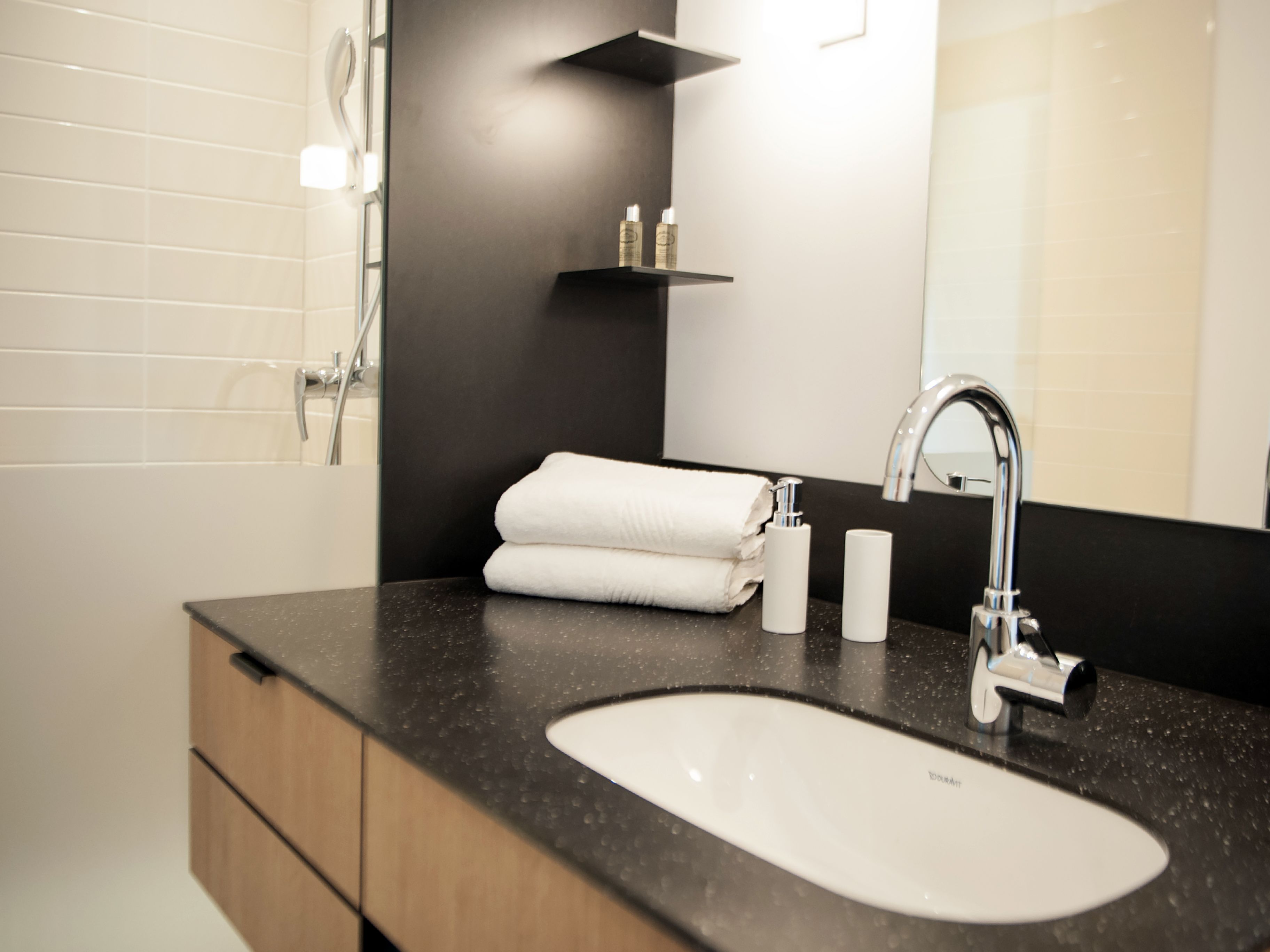 Un baño moderno con un lavamanos blanco, una encimera negra, un espejo y un perchero para toallas.