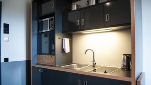 A modern kitchen with dark cabinetry, a stainless steel sink, a microwave, and a kettle. - Apartment040 (Hamburg)