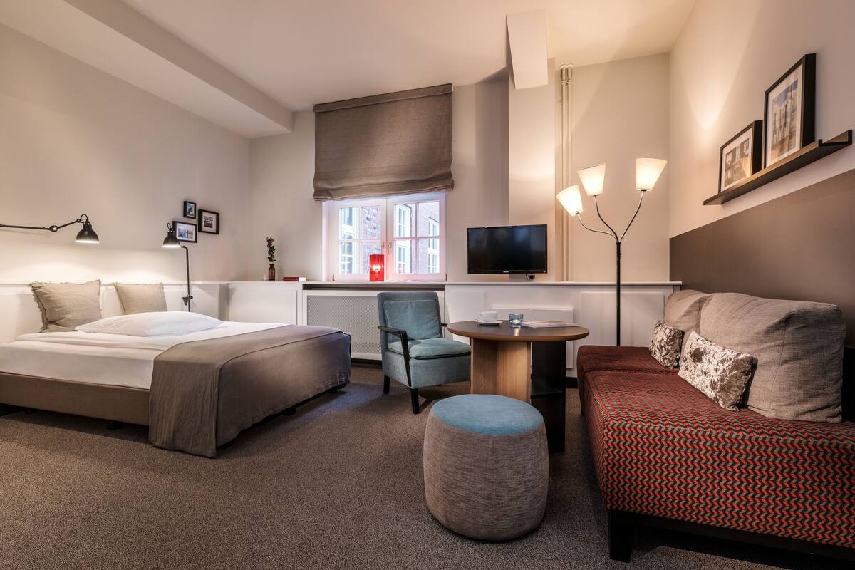 Una habitación de hotel moderna con una cama grande, un sofá, una mesita, una silla y un televisor.
