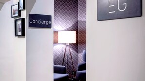A hotel corridor with a 'Concierge' sign, a 'EG' sign, framed pictures on the wall, and a lamp in the background. - Apartment040 (Hamburg)