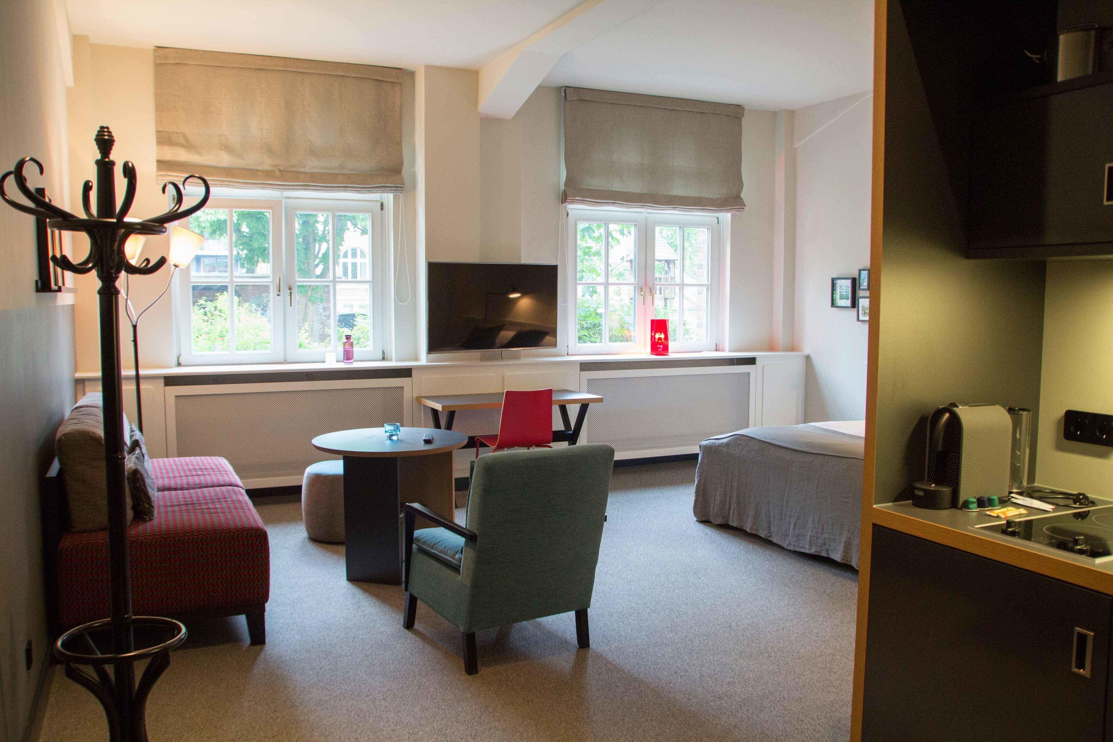 Een gezellige kamer met een bank, fauteuil en een klein tafeltje. Er is een raam met uitzicht op groen.