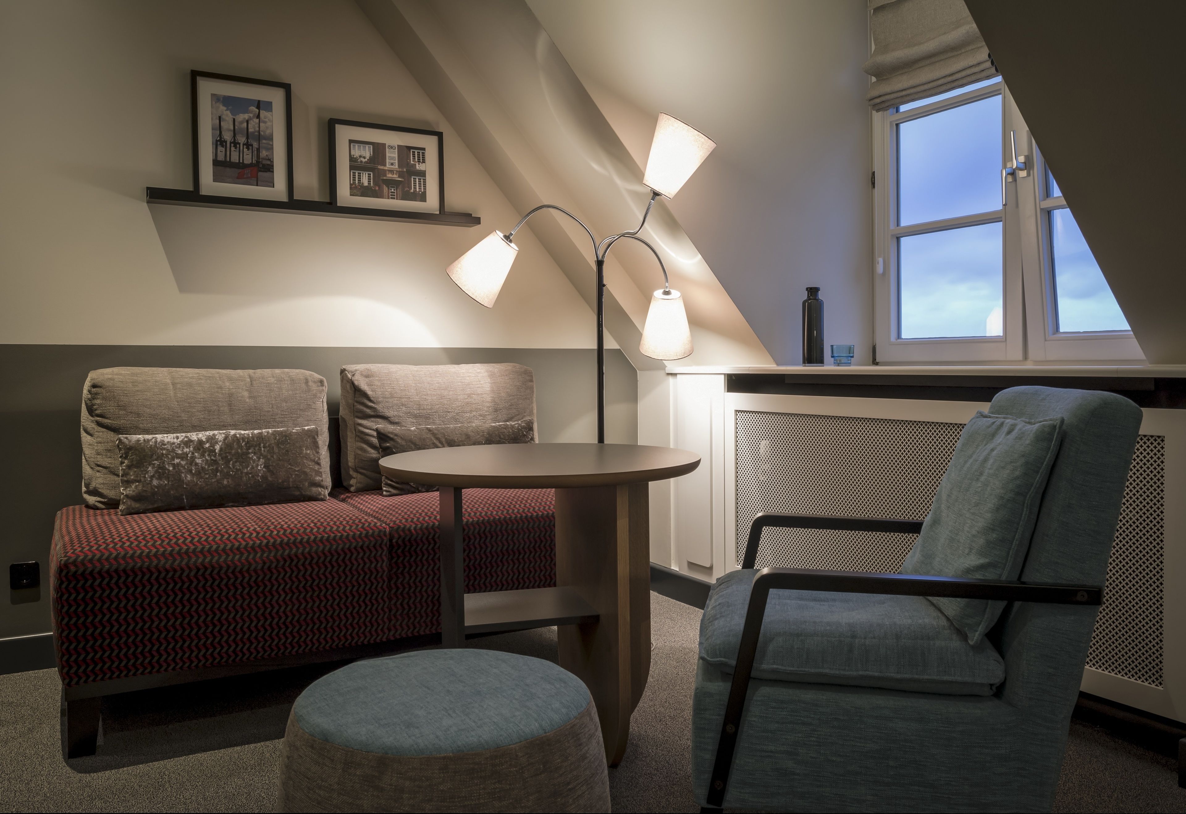 A cozy room with a red patterned sofa, a blue armchair, a round table, and a floor lamp.