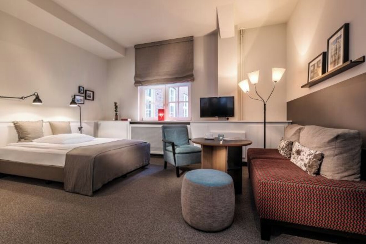 A hotel room with a bed, a sofa, a chair, a small table, and a TV.