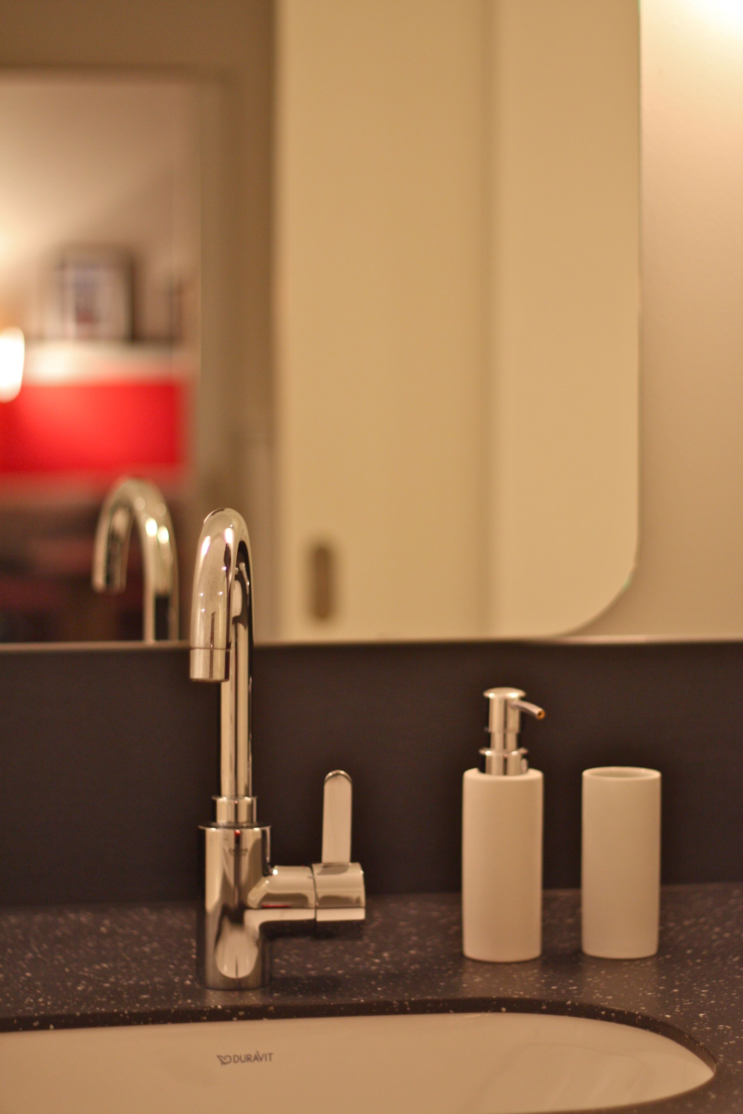 Un lavabo de bany amb un aixeta moderna, un mirall i dos dispensadors de sabó blancs.