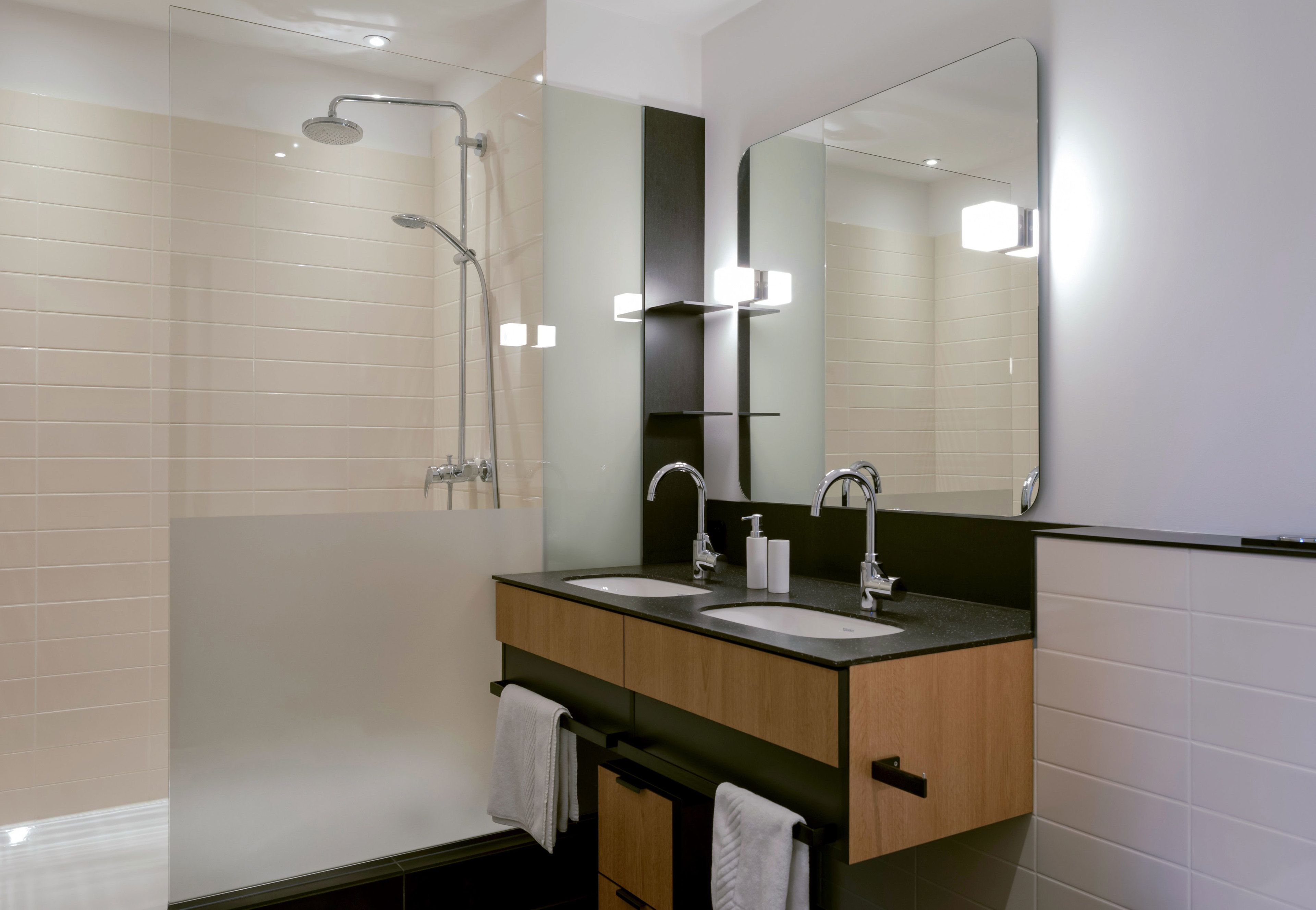Un baño moderno con dos lavamanos, una ducha y un espejo grande.