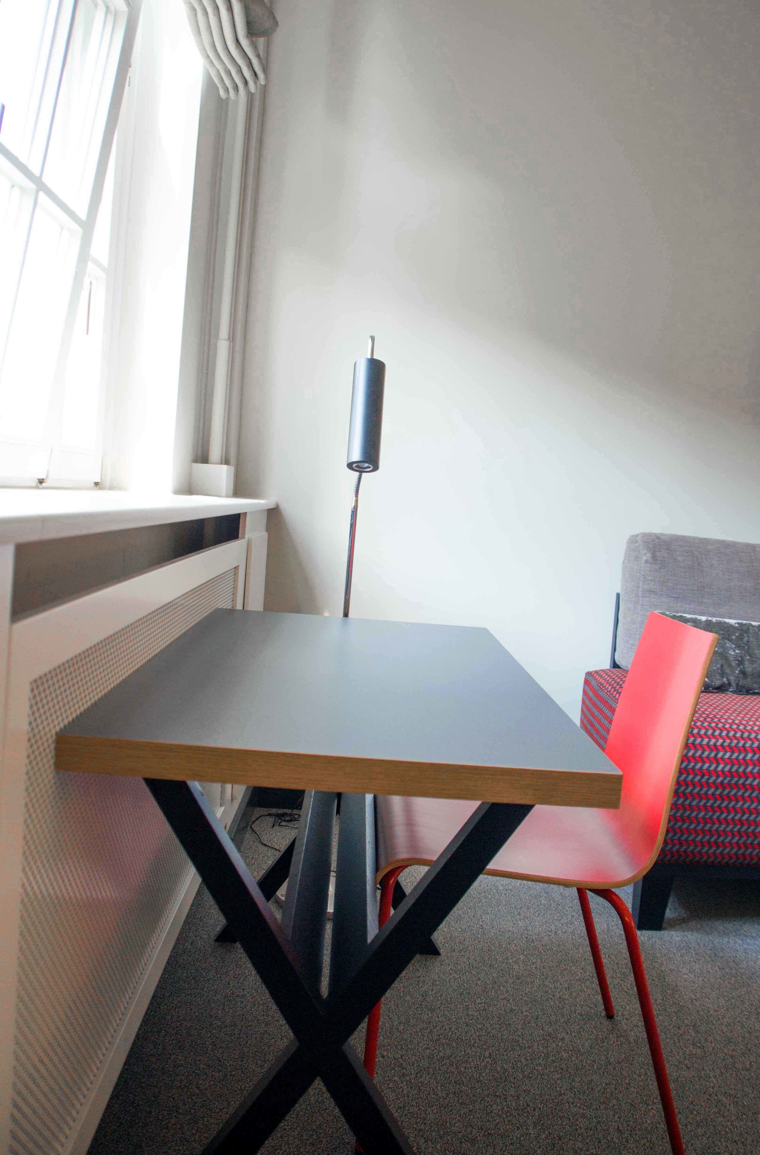 Een kamer met een tafel en een rode stoel, een radiator en een raam met gordijnen.