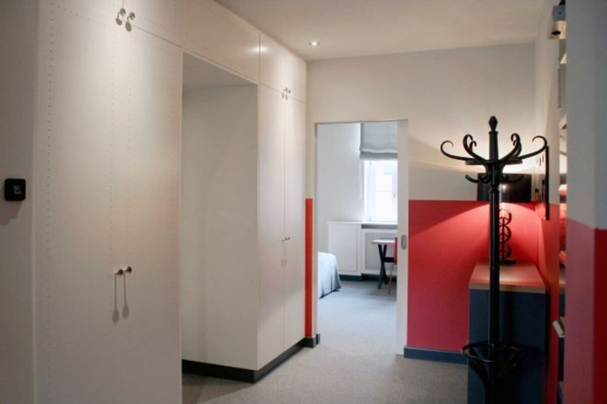 A hallway with a coat rack, a door with a handle, and a window with blinds.