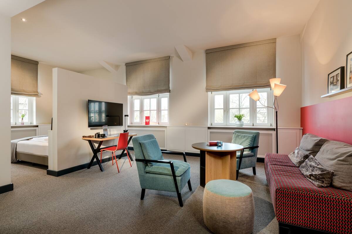 Una habitación de hotel moderna con cama, escritorio, televisor y zona de estar con sillas y sofá.