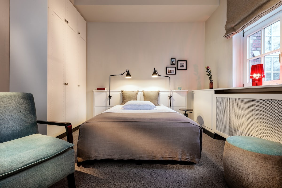 Un dormitorio con una cama, dos lámparas de noche, un ventanal y un radiador.