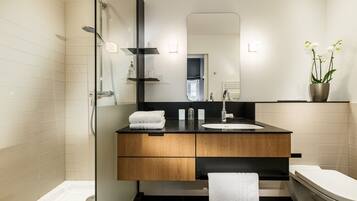 A modern bathroom with a glass-enclosed shower, a wooden vanity with a black countertop, a white sink, and a toilet.