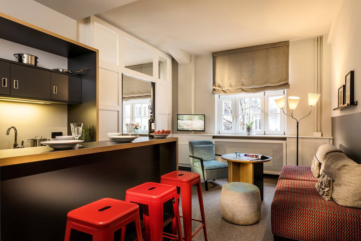 Un espacio habitable compacto con kitchenette, sofá, mesa de comedor y una silla.