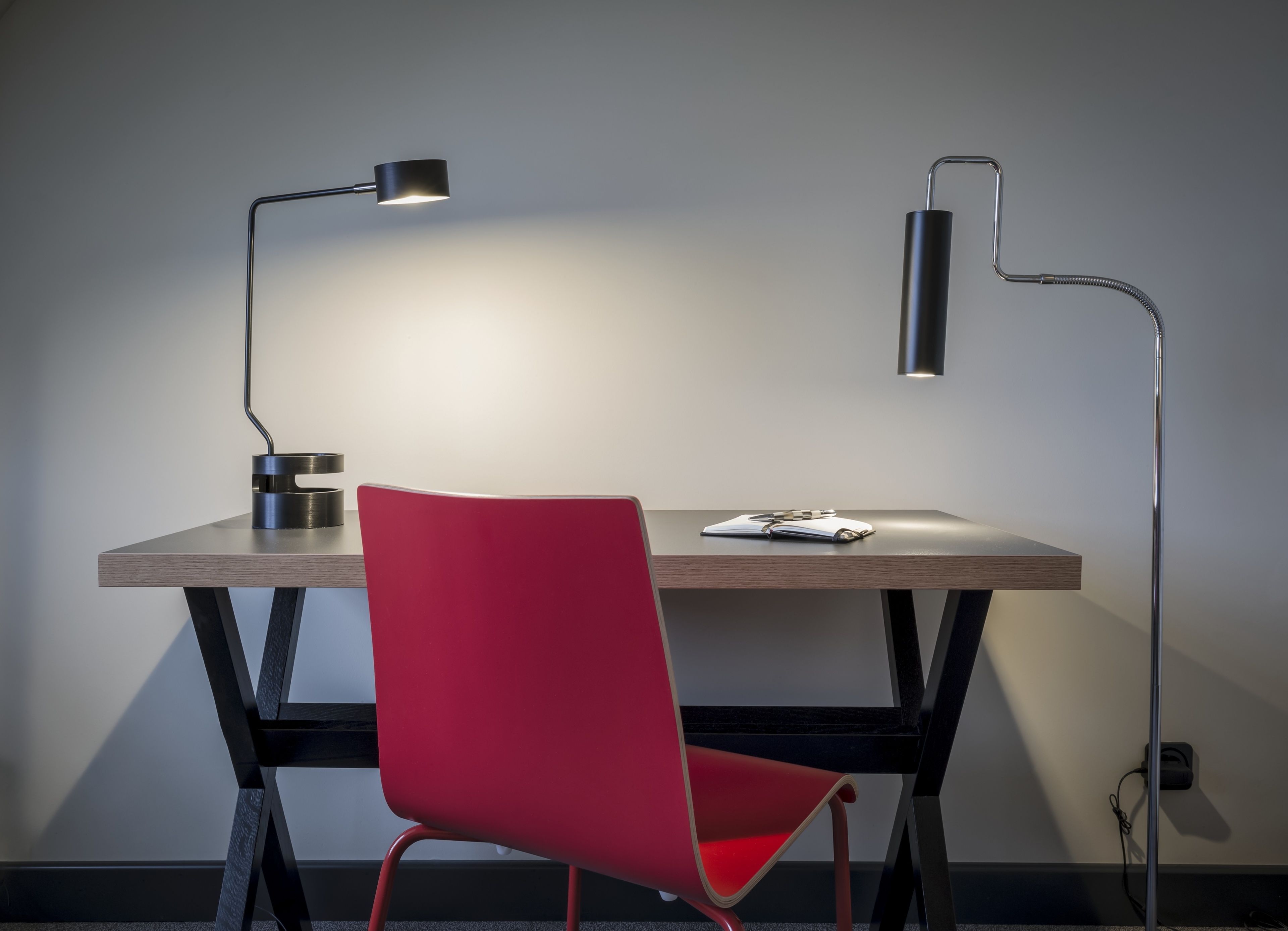 Een modern bureau met een rode stoel, twee bureaulampen en een notitieboekje.