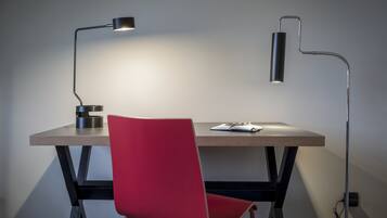 Een modern bureau met een rode stoel, twee bureaulampen en een notitieboekje.