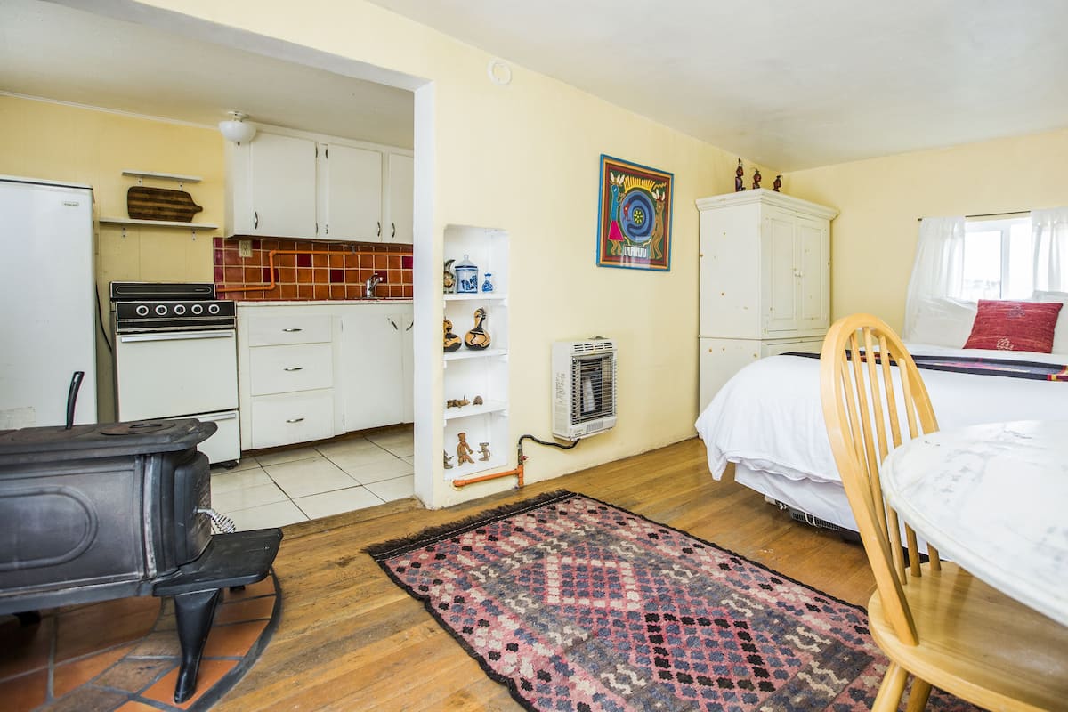 Habitación compacta con cama, silla, una mesita, estufa y radiador.