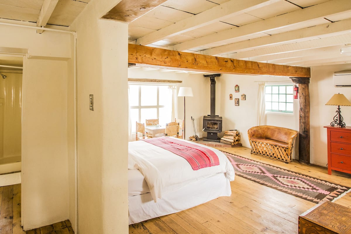 Un dormitorio amplio con una cama grande, techo de madera, chimenea y vista al exterior.