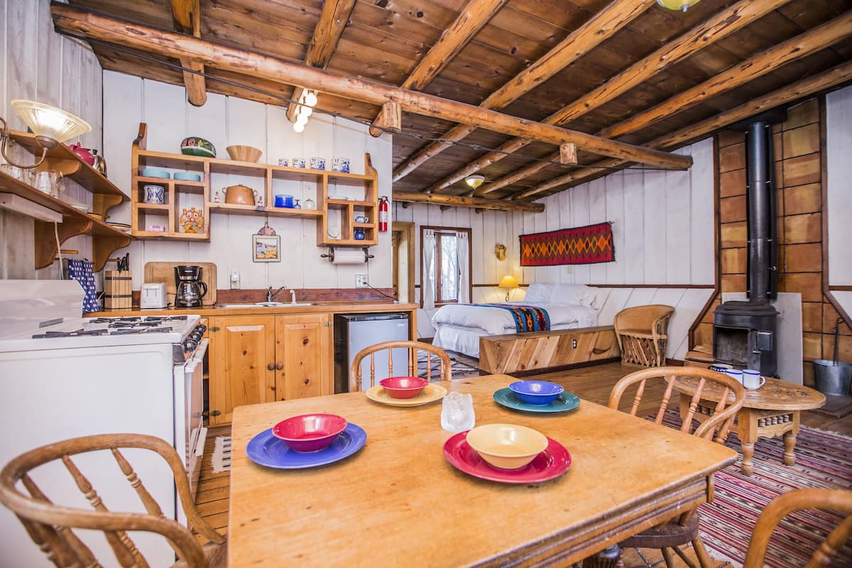 Una cocina acogedora con armarios de madera, una estufa y una mesa de comedor con platos de colores.