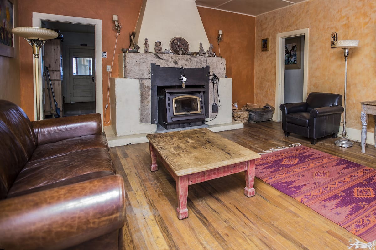 Una sala de estar con chimenea, sofá de cuero, mesa de centro de madera y alfombra estampada.