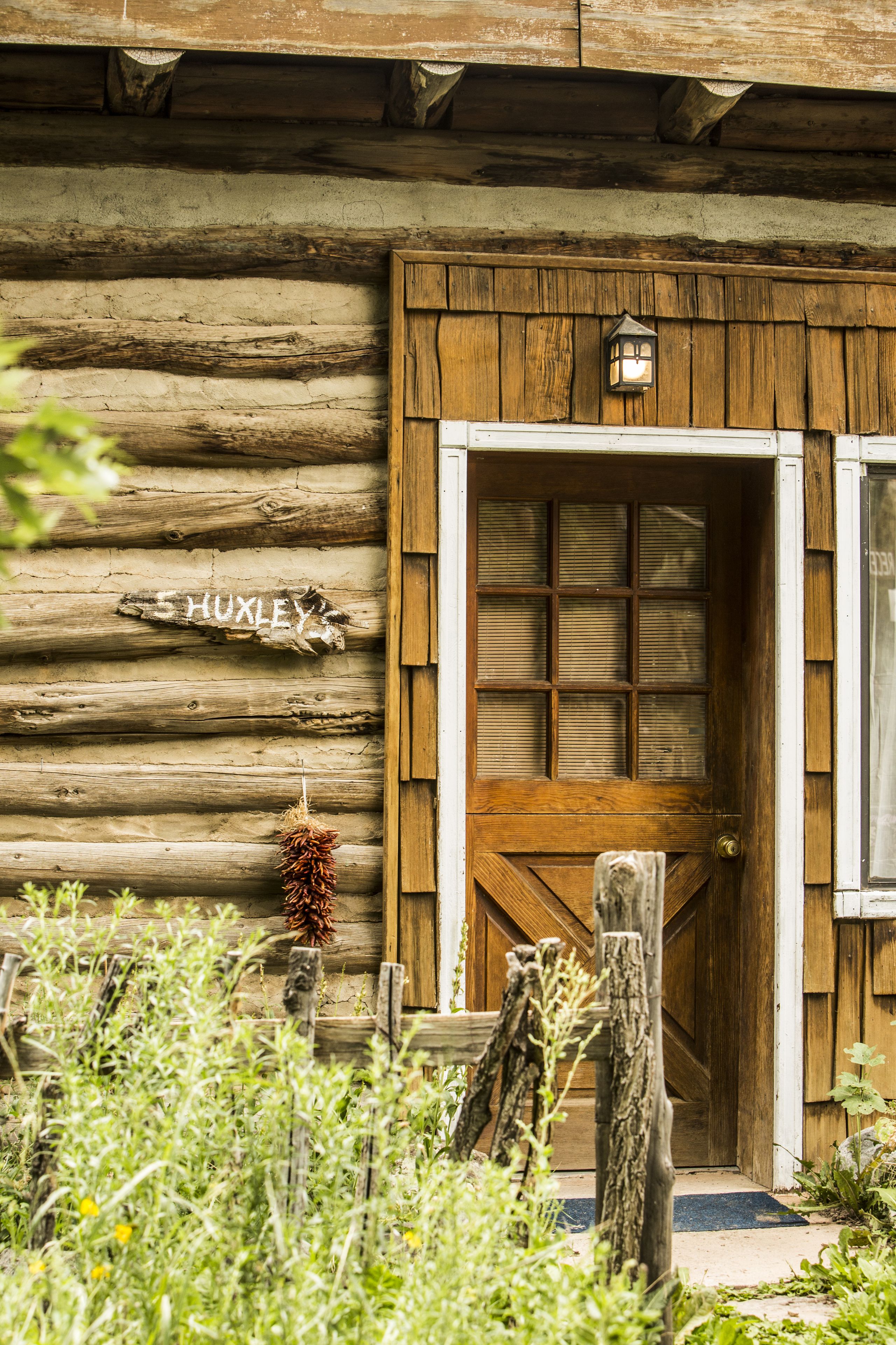 A rustic wooden cabin with a wooden door and a sign that reads "HUXLEY".