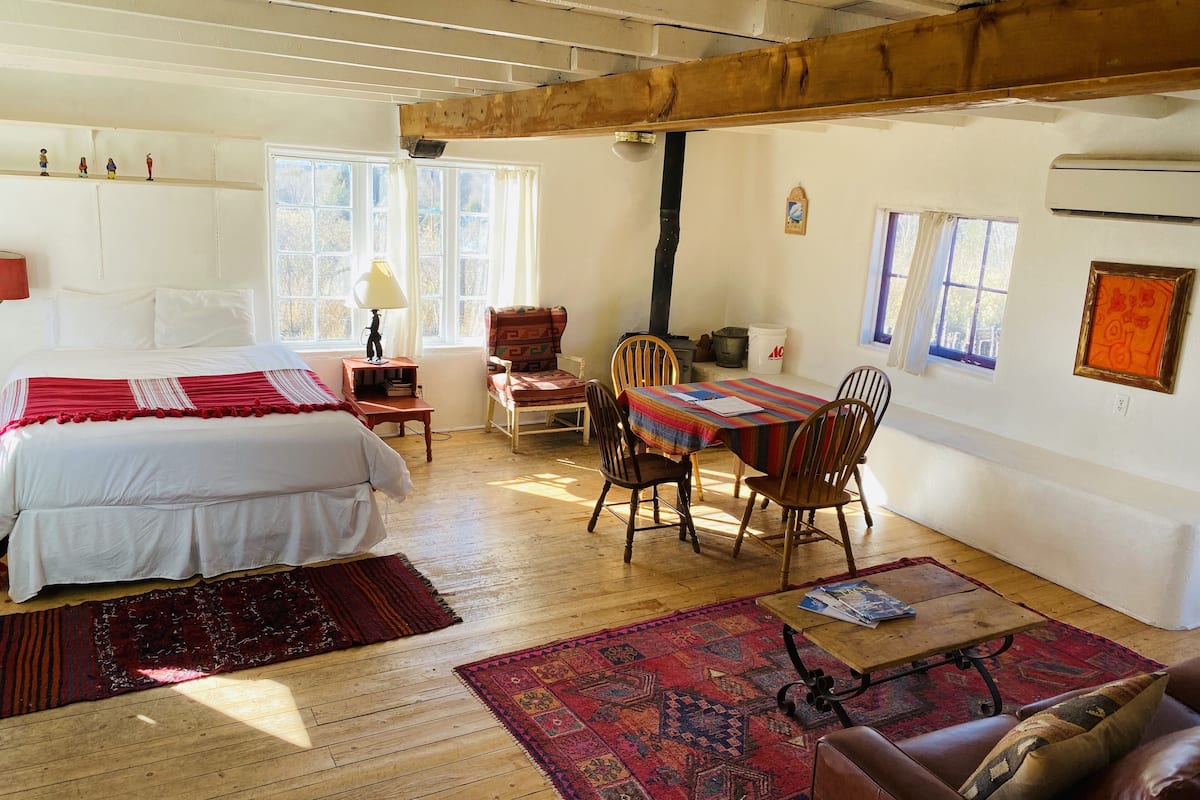 Una habitación acogedora con cama, una mesa y sillas, techo de madera y un ventanal.