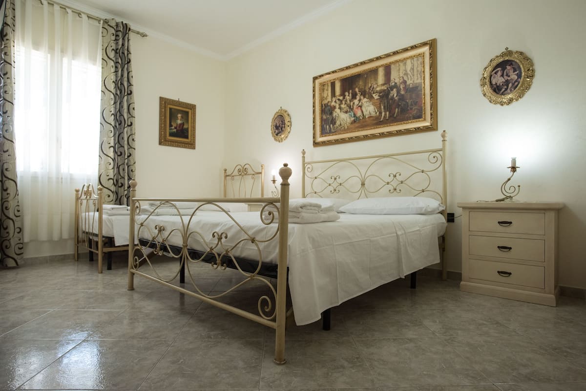Une chambre à coucher avec un lit en métal, deux tables de chevet, une commode et un grand tableau accroché au mur.