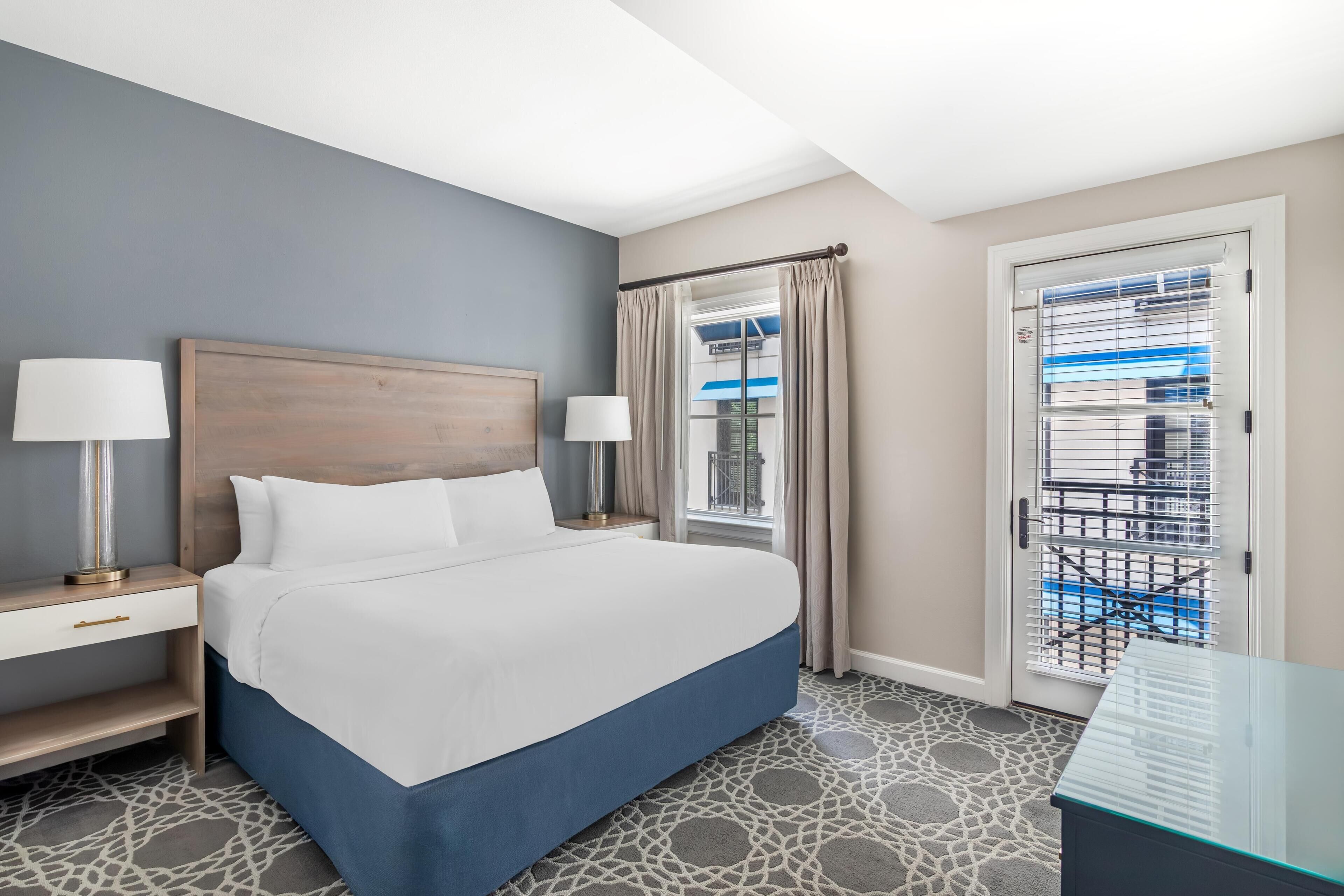 A hotel room with a bed, bedside tables, lamps, a window with curtains, and a view of the outside.