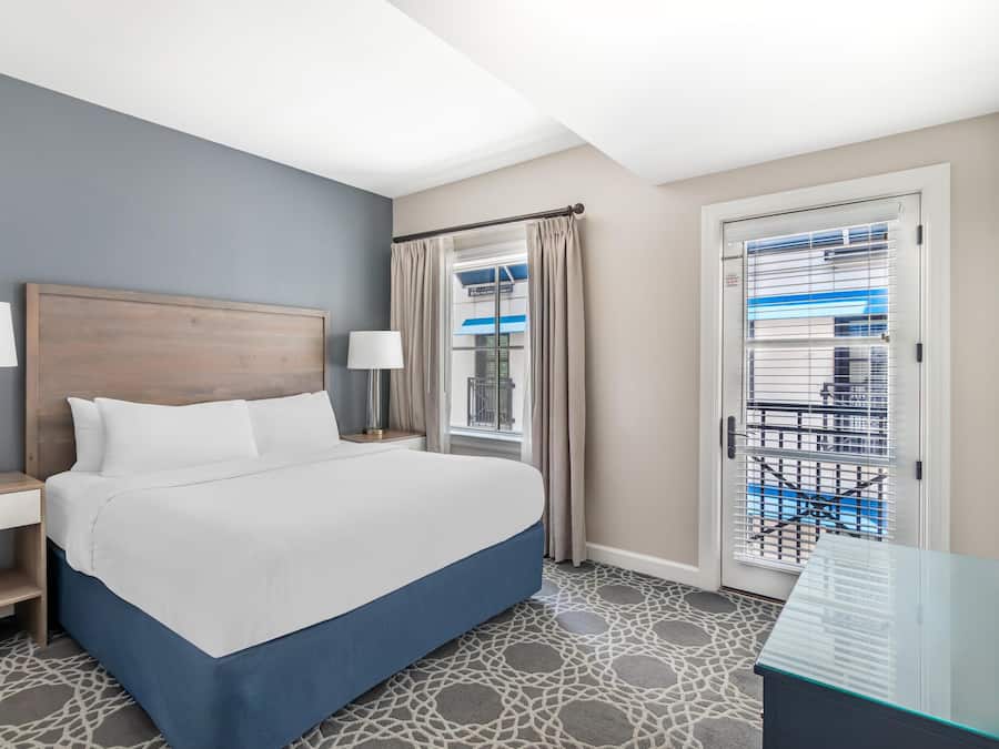 Habitación de hotel con cama, mesitas de noche, lámparas, ventana con cortinas y vistas al exterior.