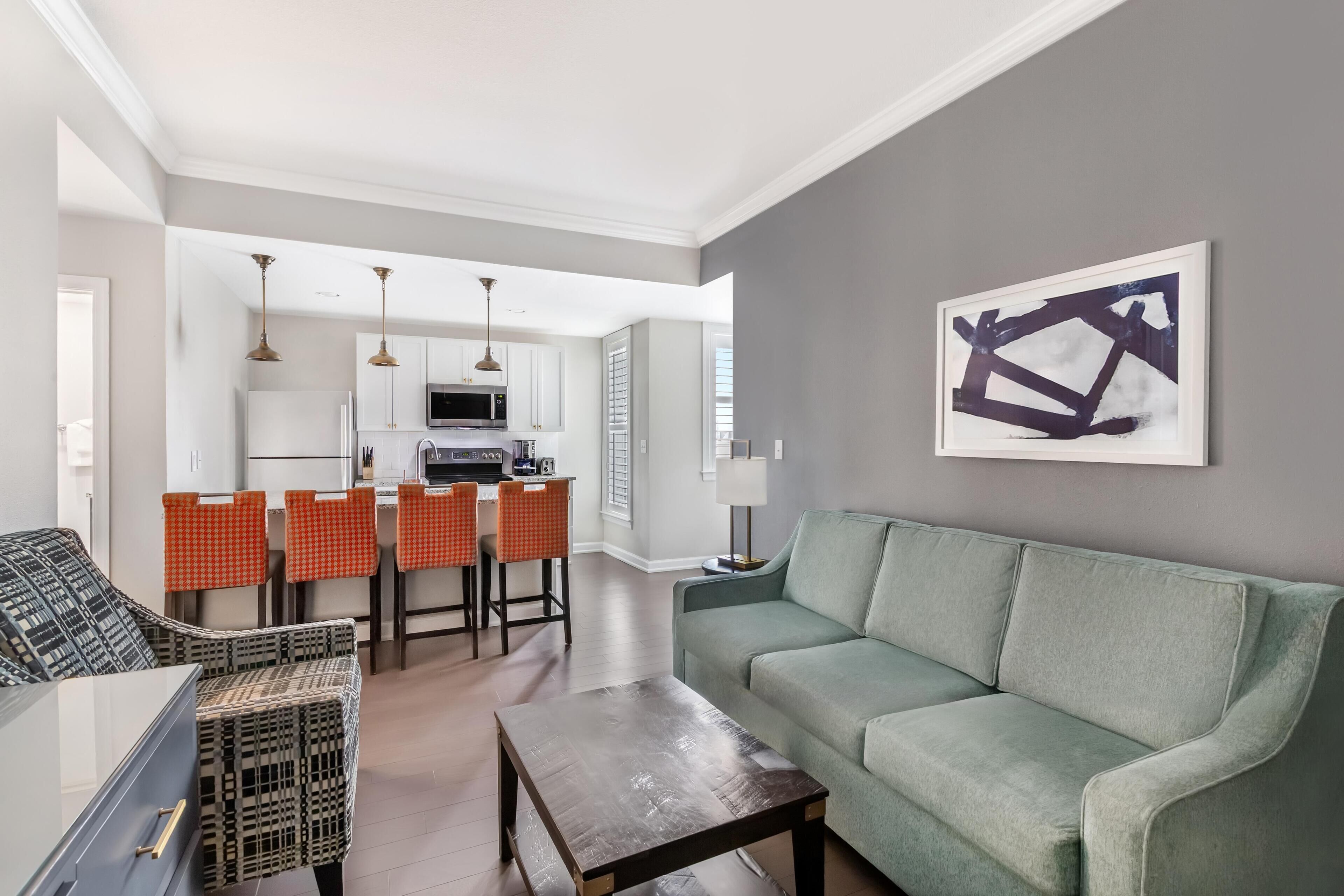 A modern living room with a green sofa, a coffee table, and a dining area with orange chairs.