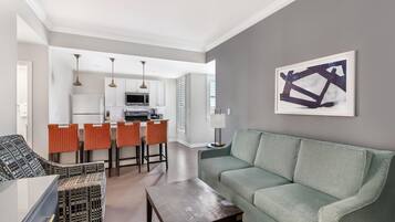 A modern living room with a green sofa, a coffee table, and a dining area with orange chairs.