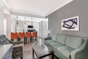 A modern living room with a green sofa, a coffee table, and a dining area with orange chairs. - Hilton Vacation Club King 583 Charleston (Charleston)