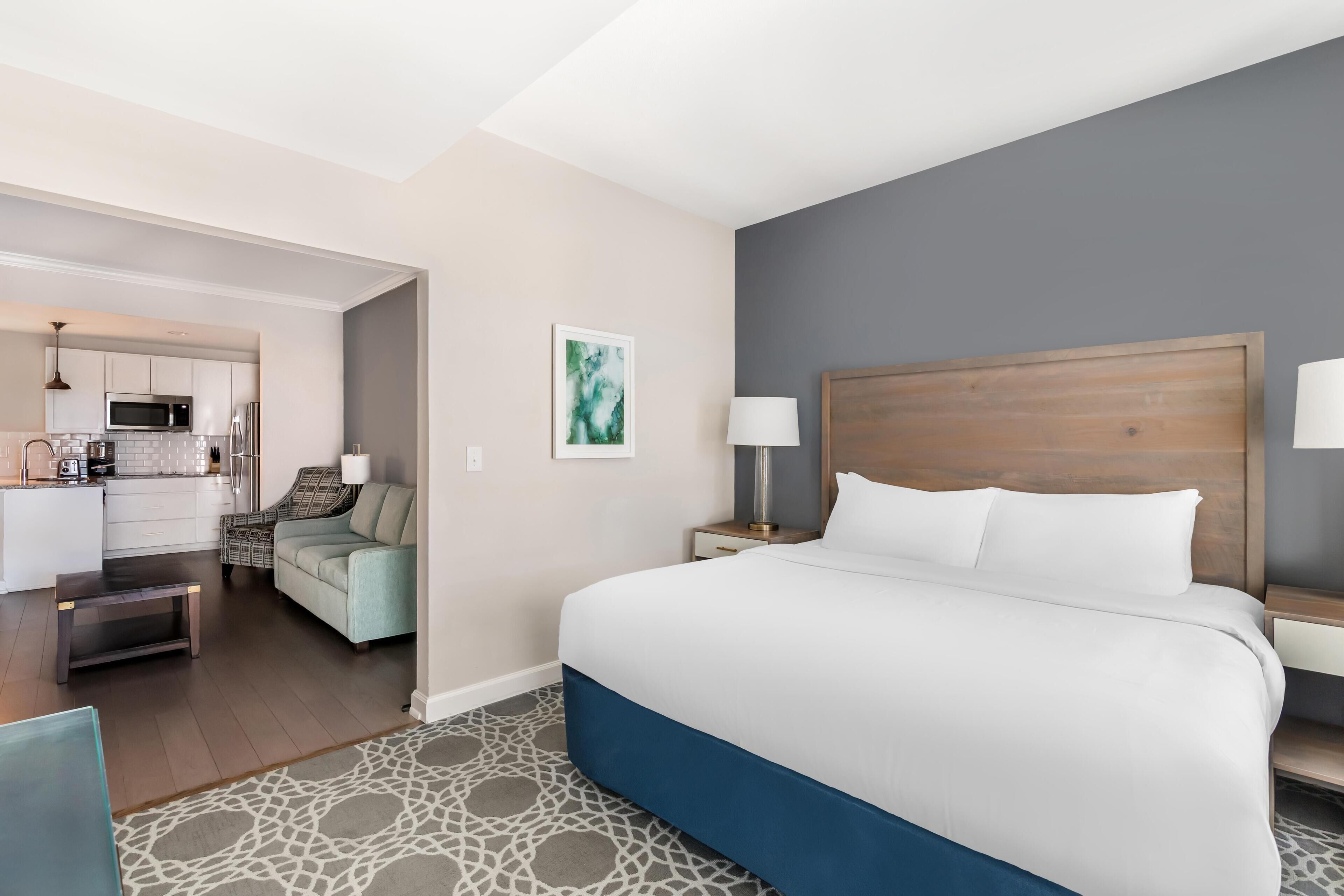 Habitación de hotel con cama, mesitas de noche, lámpara, un cuadro, kitchenette y zona de estar.