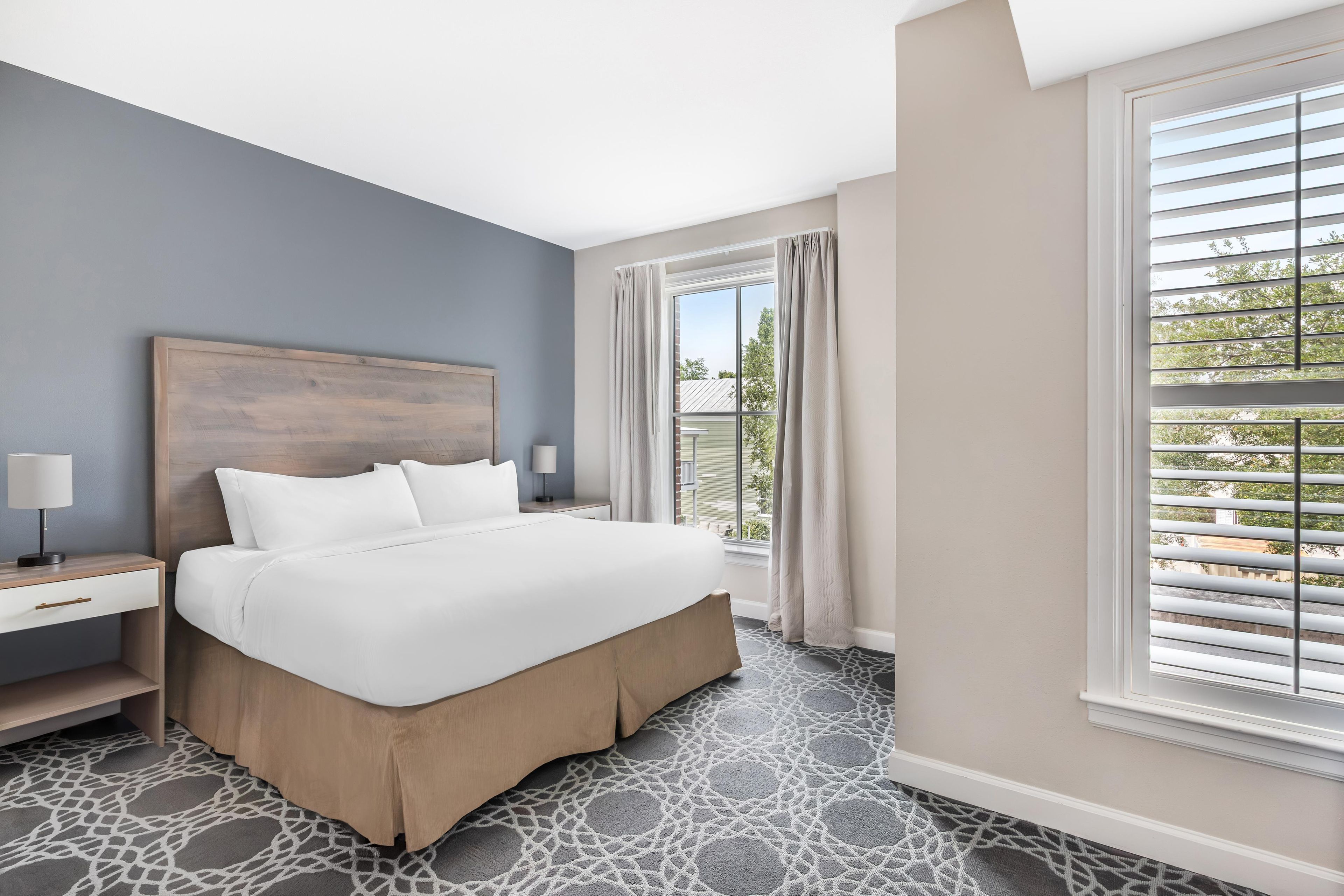 Une chambre d’hôtel avec un grand lit, une table de chevet, une fenêtre avec des stores et une vue sur l’extérieur.