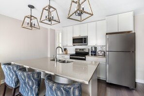 Een moderne keuken met een centraal eiland, roestvrijstalen apparatuur en een opvallende geometrische hanglamp.