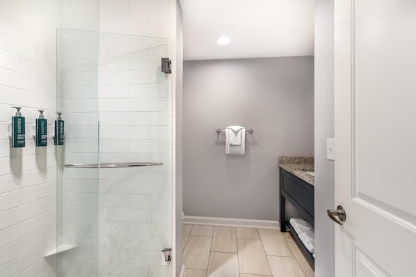 A bathroom with white tiled walls, a shower with a glass door, a towel rack, and a sink with a granite countertop. - Hilton Vacation Club King 583 Charleston (Charleston)