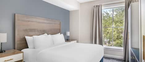Una habitación de hotel con una cama grande, una mesita de noche, una lámpara y un ventanal con cortinas.