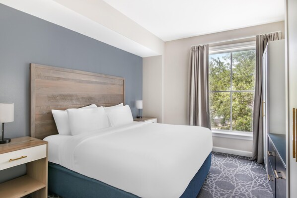 A hotel room with a large bed, a nightstand, a lamp, and a window with curtains.