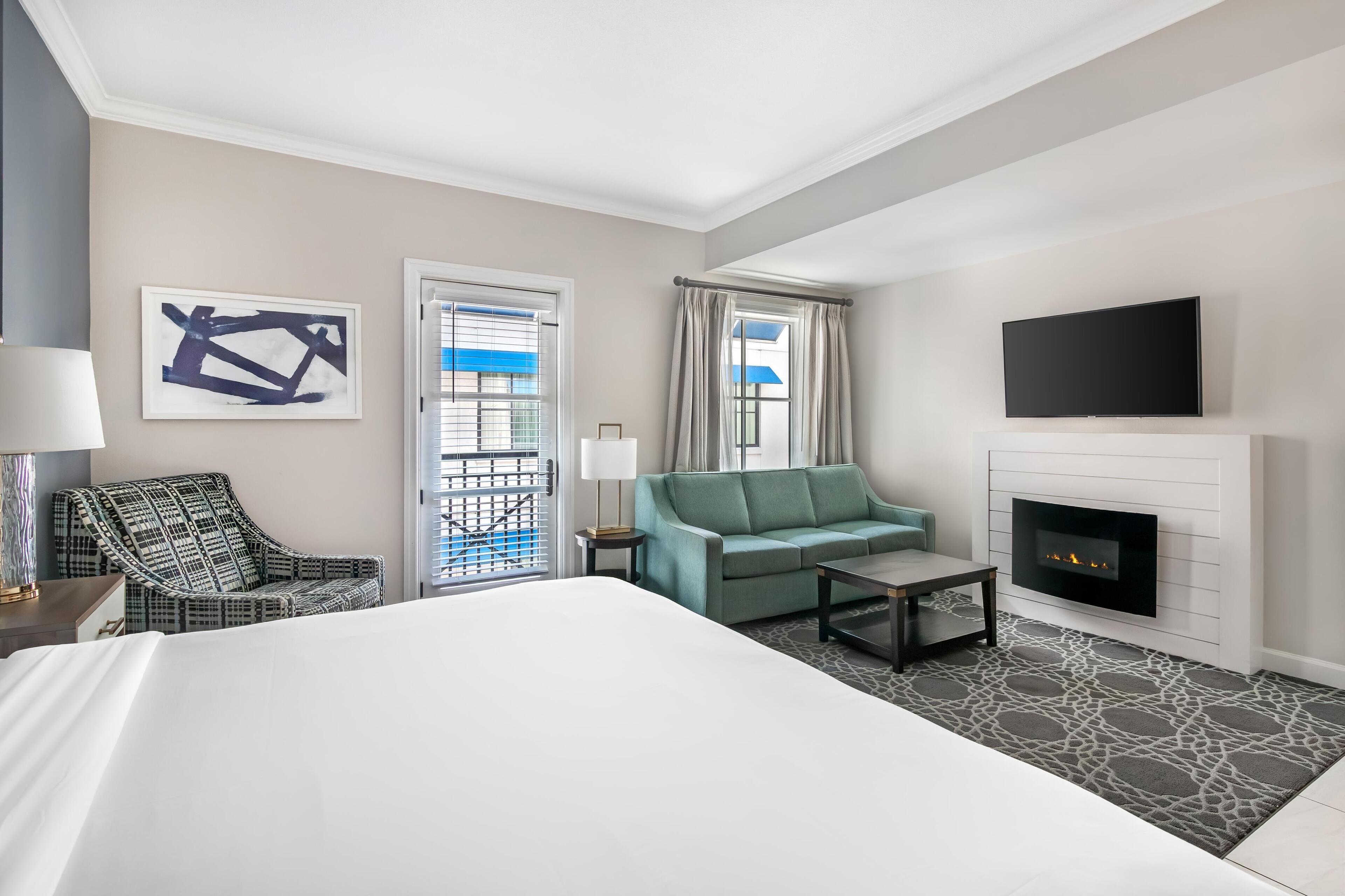 Una habitación de hotel con cama, sofá, sillón, televisor y chimenea.