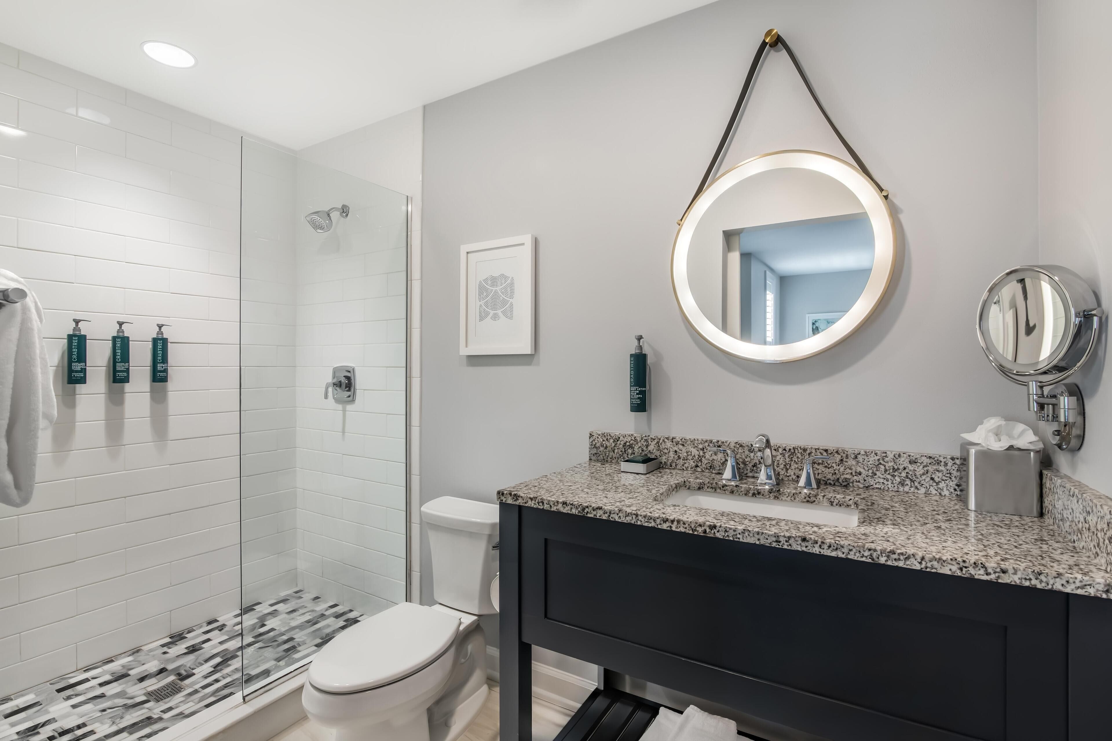 A modern bathroom with a shower, toilet, vanity, and a mirror with a light.