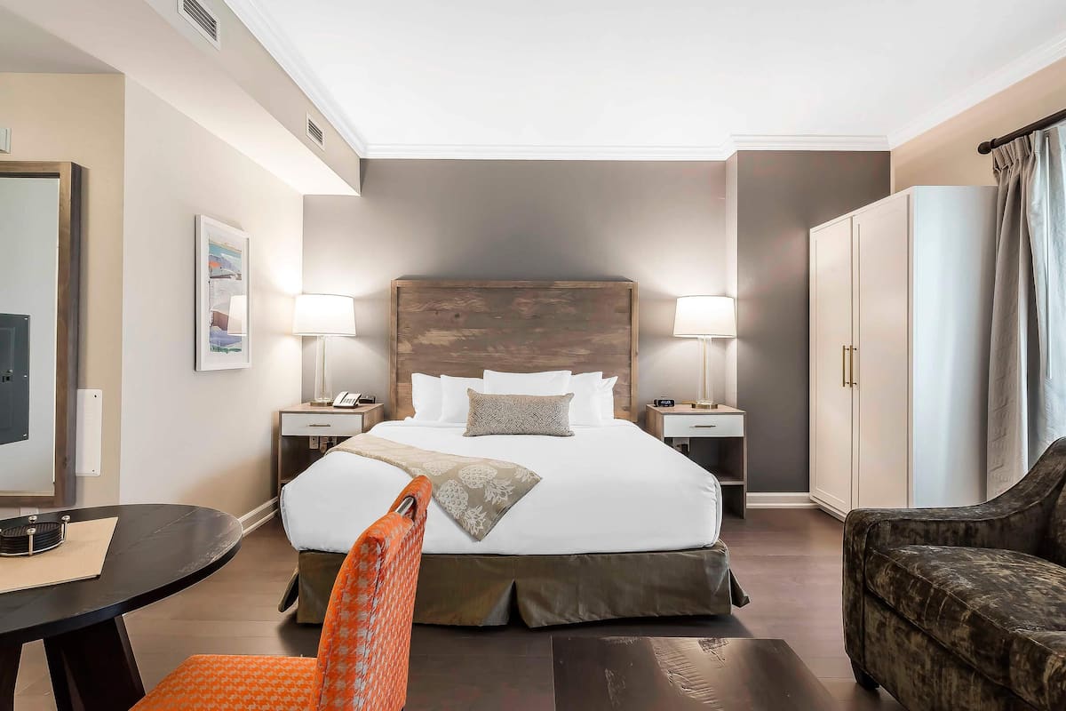 Una habitación de hotel con una cama grande, mesitas de noche, un escritorio, una silla y un armario.