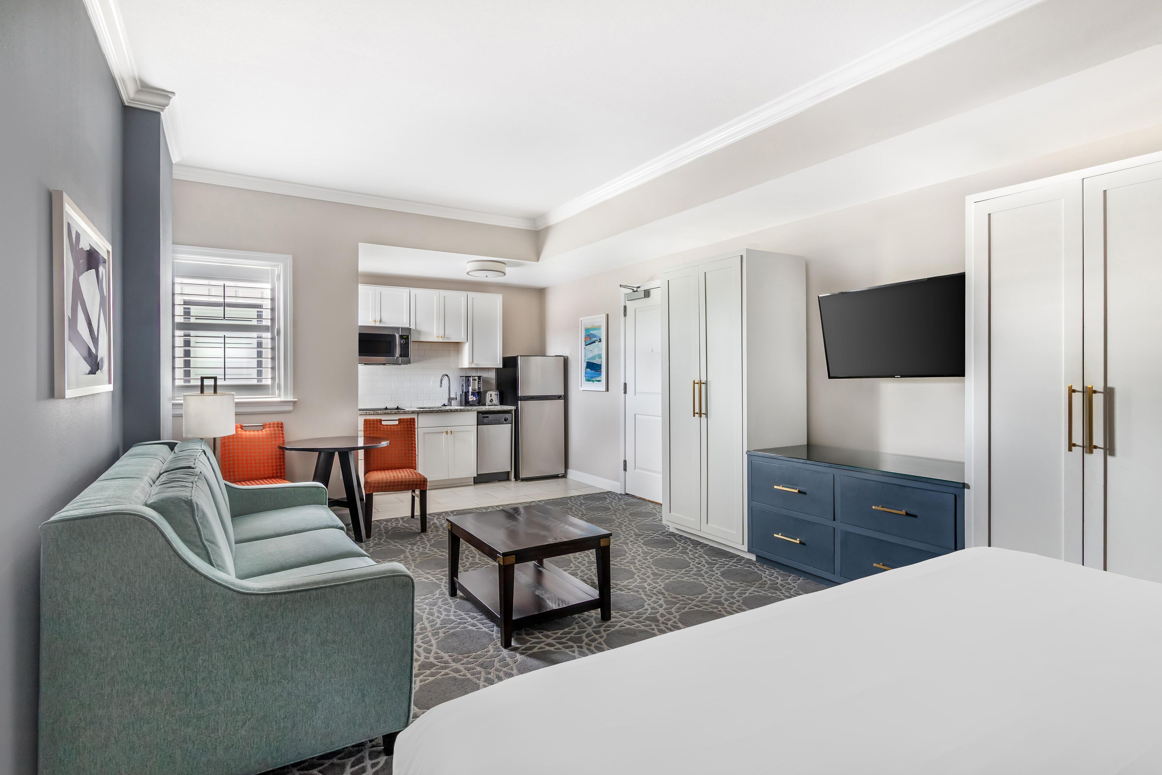 Habitación de hotel con cama, sofá, mesa de comedor, cocina y televisor.