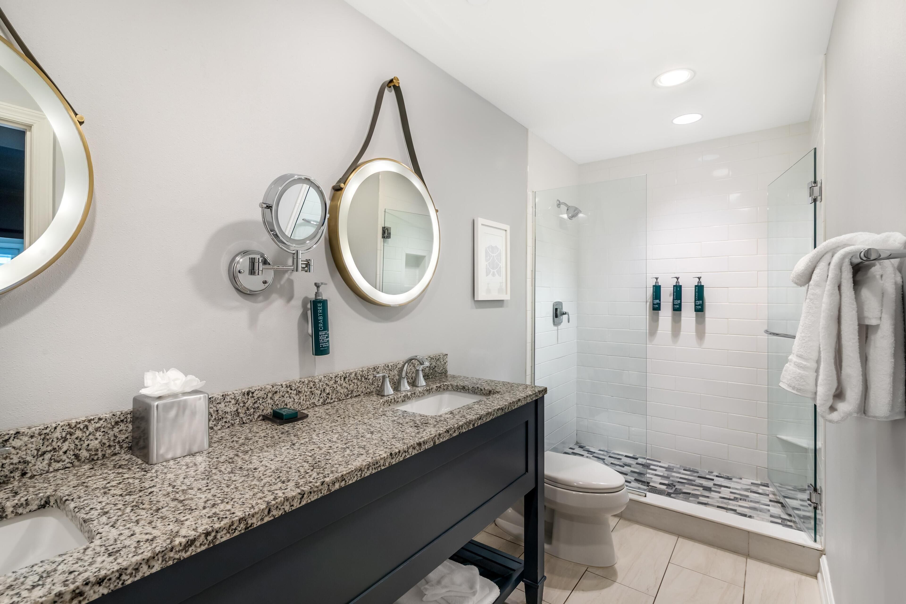 Une salle de bain moderne avec un comptoir en granit, un meuble-lavabo, un grand miroir, une douche et des toilettes.