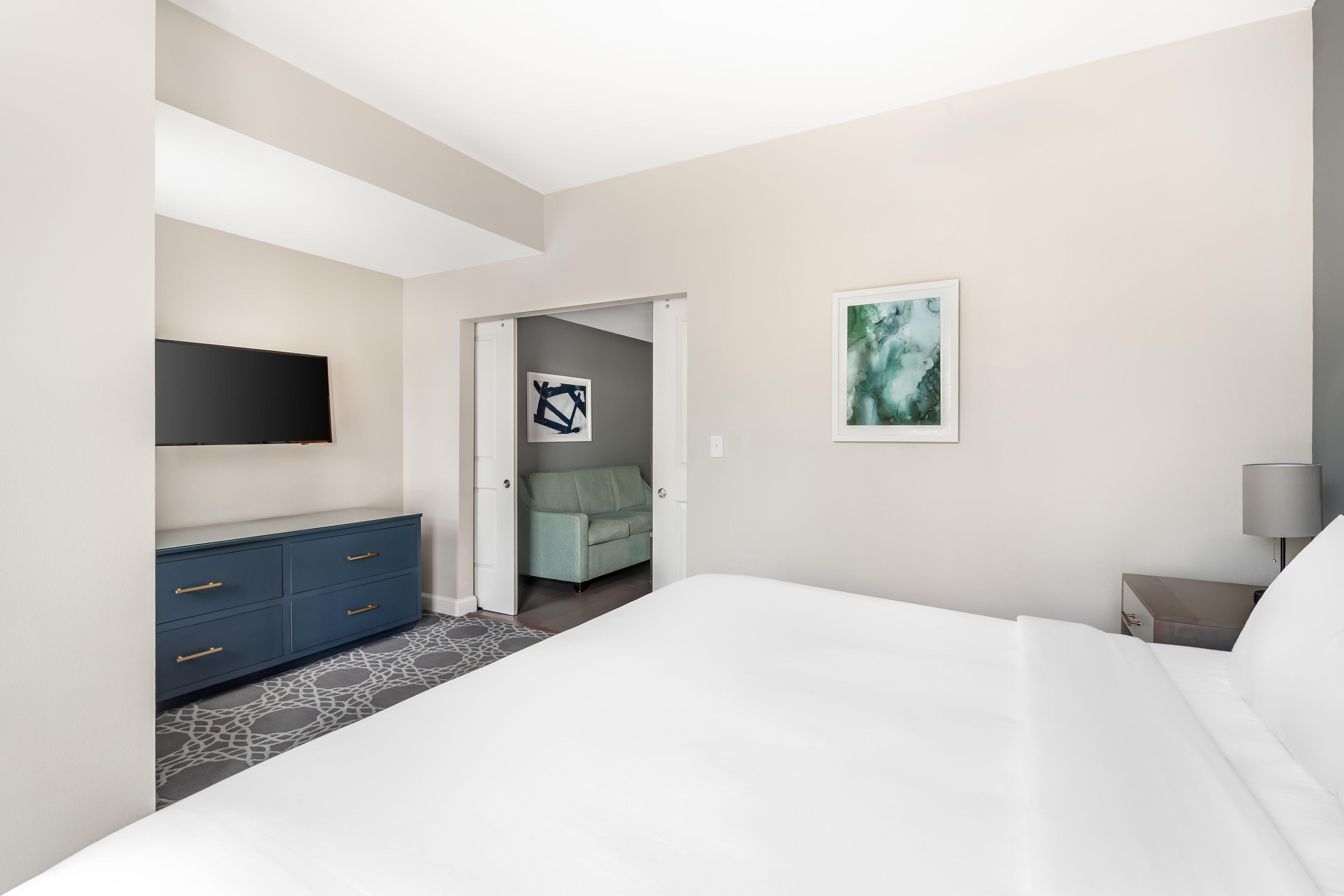 A hotel room with a bed, a dresser, a TV, and artwork on the walls.