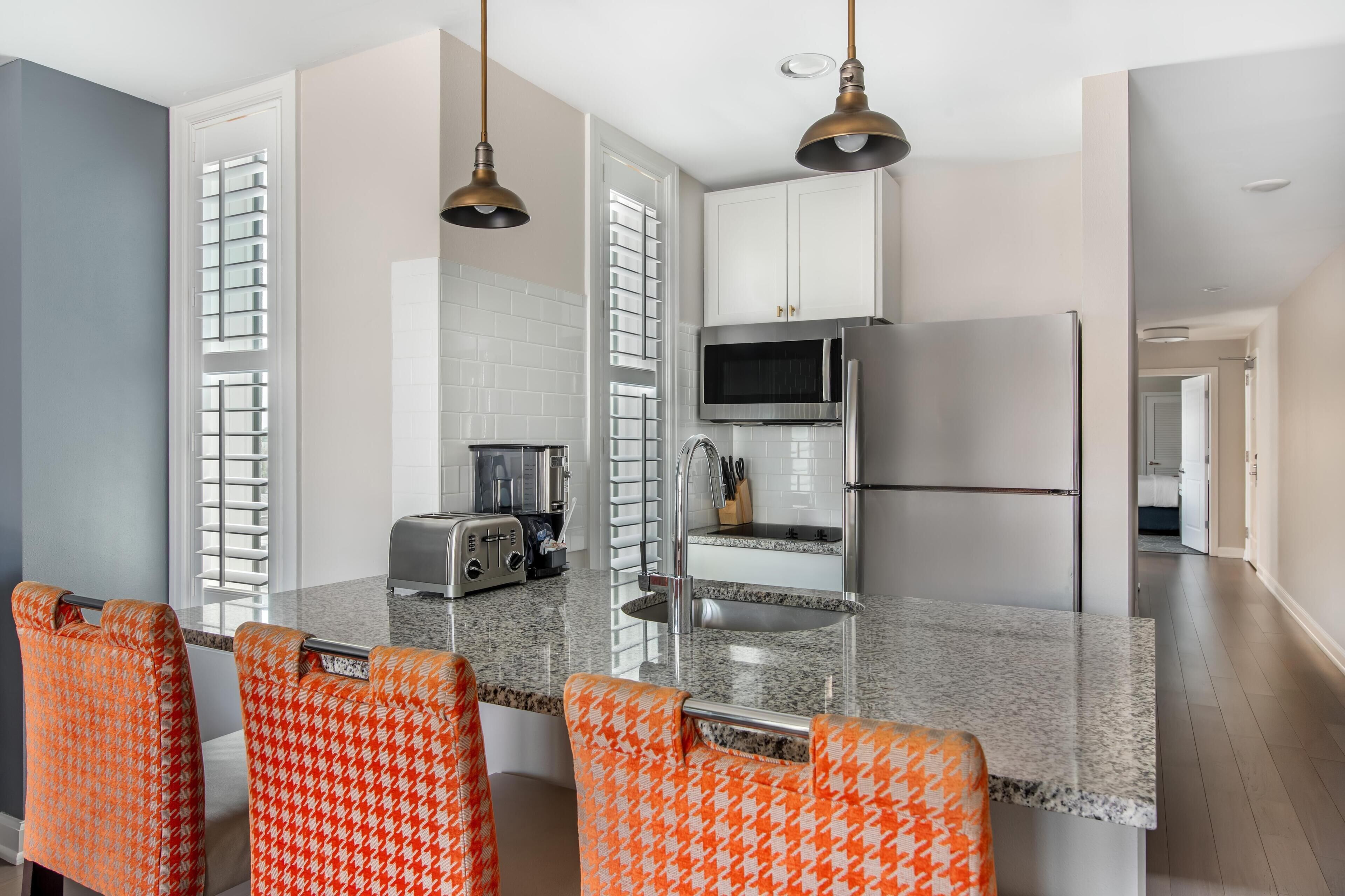 A modern kitchen with a granite countertop, stainless steel appliances, and houndstooth patterned chairs.