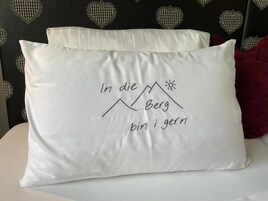 Almohada con diseño de montaña y sol, y texto en un idioma extranjero.